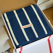 Navy towel with white stripes and 'coolcabanas' logo in a box on a wooden floor.